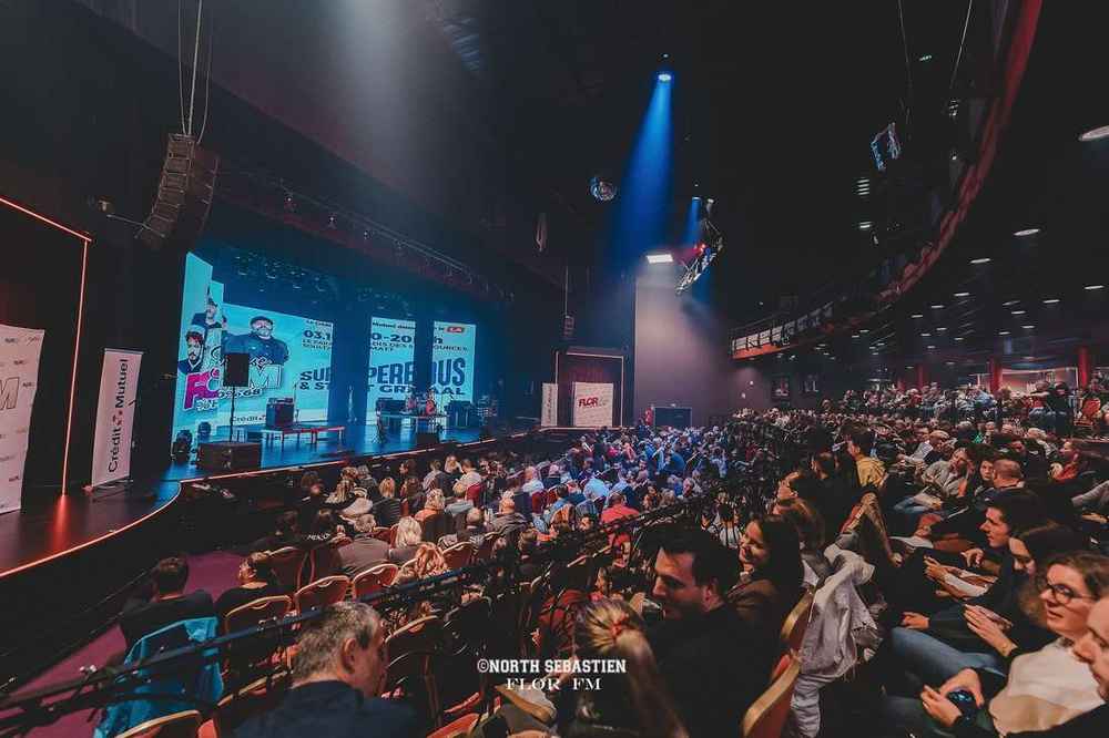 Salle de spectacle remplie, écran géant et scène éclairée